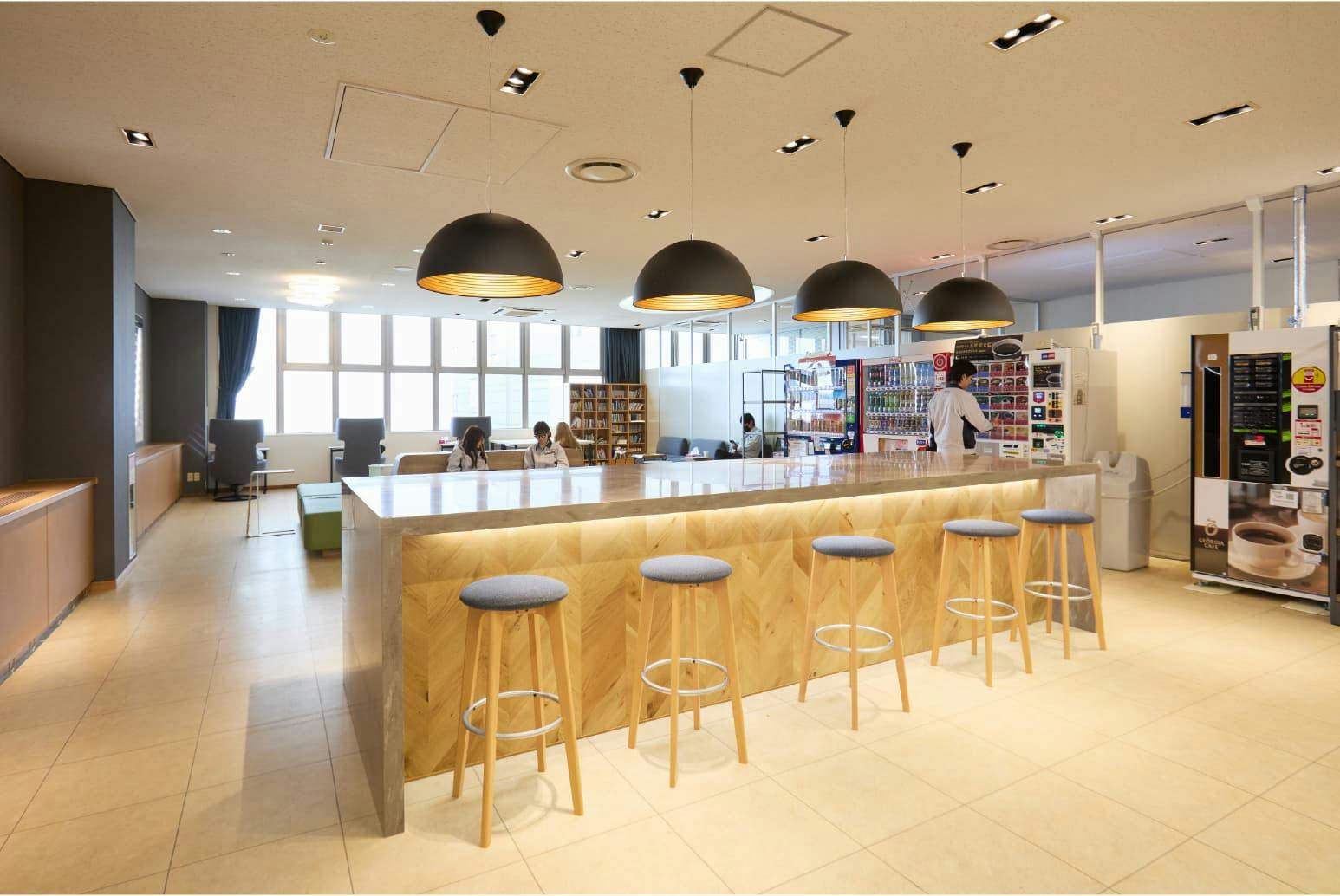 日東電工株式会社 様の事例写真／[3F リフレッシュエリア（社員食堂）]自販機と、ペンダントライトが照らすハイカウンターを設置。読書や仮眠、コーヒーブレイクをして気分転換し、業務へ向かうエネルギーをチャージする場になっています。